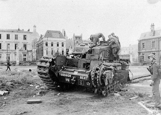 Photographie en noir et blanc – Plusieurs soldats allemands rampent jusqu’à un char d’assaut Churchill abandonné dans un square à Dieppe. L’un des côtés du char a été lourdement endommagé.